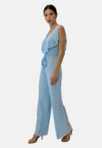 Ljust blå plisserad jumpsuit med volangärmar, en åtsittande midja och vida byxor, som har ett knytbälte och en slät textur.