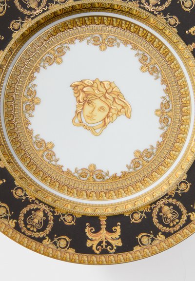 Keramický tanier s bielym stredom a zlatým motívom Medúzy, obklopený zdobenými zlatými a čiernymi kvetinovými vzormi a detailmi.