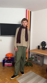 Beige skjorte med knapper, mørkerød skjerf, grønne cargo-bukser, svarte slip-on sko. Står i et rom med moderne innredning og en plante.