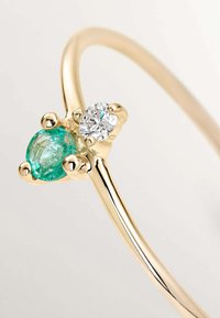Anillo de oro con una piedra preciosa azul-verde y un diamante transparente, ambos engastados en garras redondeadas, con una banda lisa y pulida.