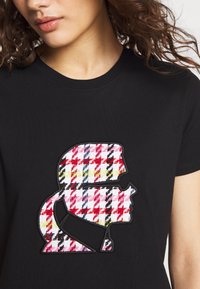 Czarna koszulka z krótkim rękawem z haftowanym wzorem w wielokolorową kratę, podkreślonym czarnym konturem. Okrągły dekolt.