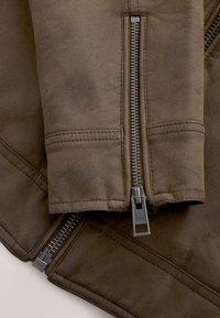 Close-up van bruine leren jas-mouwen met metalen ritsen en gedetailleerde stiksels.