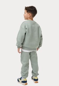 Sudadera verde claro y joggers a juego en tela suave, con puños y dobladillo acanalados. Zapatillas con acentos en azul, amarillo y blanco.