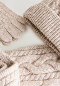 Strickhandschuhe und ein Schal aus weichem, hellem beige Garn mit einem Zopfmuster und Rippdetails, die eine strukturierte Oberfläche präsentieren.
