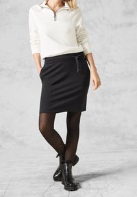 Sweat-shirt blanc à col zippé associé à une jupe crayon gris foncé avec taille à cordon de serrage et poches latérales, porté avec des bottines noires.