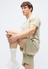 Μπεζ αθλητική μπλούζα και σορτς, υφασμάτινη υφή, σορτς μήκους έως το γόνατο με πλευρικές σχισμές, συνδυασμένο με λευκές κάλτσες και αθλητικά παπούτσια.