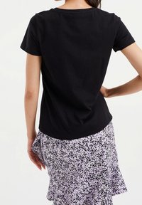Černé bavlněné tričko s krátkým rukávem, kulatým výstřihem a volným střihem, v kombinaci s fialovou sukní s černými skvrnami.