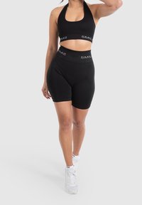 Musta urheilullinen crop-top ja korkea vyötärö shortsit, jotka on valmistettu sileästä kankaasta ja joissa on logonauha. Yhdistetty valkoisten tennareiden ja nilkkasukkien kanssa.