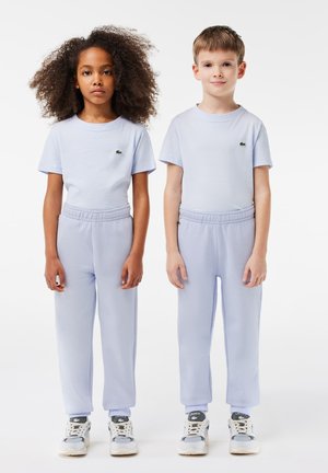 T-shirts en coton bleu clair et sweatpants assortis. Pas de motifs. Les sweatpants ont des ceintures élastiques. Les deux enfants portent des baskets blanches avec des accents gris.