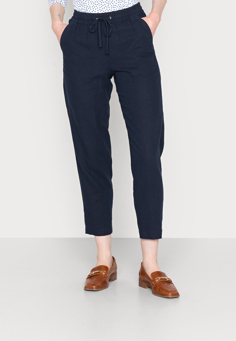 Pantalon fuselé bleu marine, léger, taille élastique avec cordon de serrage, doté de poches latérales, associé à des mocassins marron.
