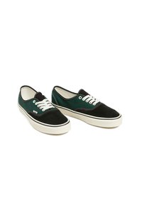 Matala kengät, joissa on musta mokkanahka varvas, vihreä leopardikuosi sivuilla, valkoiset nauhat ja valkoiset kumipohjat valkoisella taustalla.