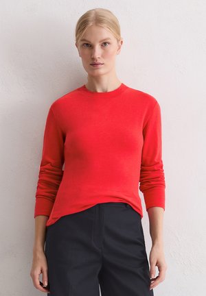 Czerwona koszulka z długim rękawem i okrągłym dekoltem, wykonana z miękkiego materiału. Do tego ciemne, dopasowane spodnie o wąskim kroju.