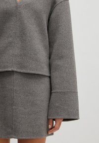 Grauer Wollpullover mit tiefem V-Ausschnitt und weiten Ärmeln, kombiniert mit einem passenden, figurbetonten Rock. Verfügt über eine weiche Textur und klare Linien.