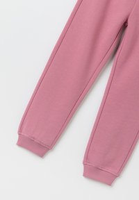 Bukser i blød lyserød stof med en tapered design og ribbede manchetter ved anklerne. Glat tekstur uden synlige mønstre eller udsmykninger.
