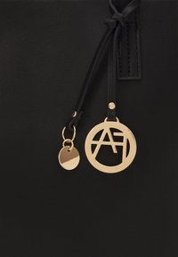 Mustat nahkakassit, jossa on tyylikäs muotoilu. Sisältää kultaisen ympyrätagin, jossa on "AF"-logo, sekä pienemmän pyöreän charm'an. Silkkinen pinta.