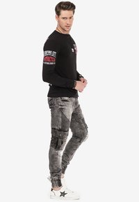 Chemise noire à manches longues avec imprimé blanc et rouge, associée à un pantalon de jogging gris texturé de style cargo avec des poches cargo et des accents rayés.
