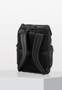 Zaino nero in pelle con spallacci in rete imbottita e design elegante. Presenta diverse tasche con zip e una forma ergonomica.