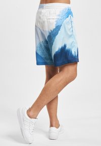 Plavkové šortky světle modré barvy s abstraktními tmavě modrými vlnovými vzory. Elastický pas, hladká látka a detail zadní kapsy.