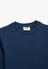 Marineblauwe thermoshirt voor kinderen met een gestructureerd wafeltricot patroon. Heeft een ronde halslijn en een label met merkinformatie aan de binnenkant.