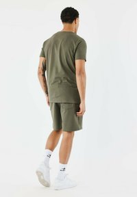 T-shirt en coton vert olive à manches courtes, associé à un short assorti. L'ensemble présente une coupe décontractée et un design minimaliste.