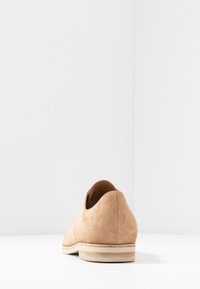 Beige suède schoen met een ronde hak, lage snit en lichte rubberen buitenzool. Heeft een gladde textuur en een eenvoudig ontwerp zonder extra hardware.