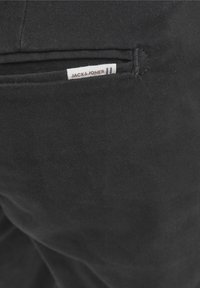 Svarta tygbyxor med en bakficka som har en etikett med texten "JACK & JONES." Materialet verkar slätt med minimal textur.