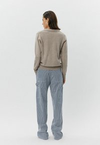 Maglione beige lavorato a maglia con orlo a costine abbinato a pantaloni cargo larghi a righe blu e bianche, dotati di tasche laterali e dalla vestibilità rilassata.