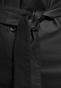 Abito in tessuto nero con cintura legata in vita, caratterizzato da una superficie liscia, bottoni e una silhouette pulita che mette in risalto elementi di design semplici.