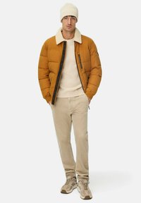 Oranje donsjack met een crèmekleurige schapenvachtkraag, crèmekleurige kabelgebreide trui, beige corduroy broek en lichtbruine sneakers.