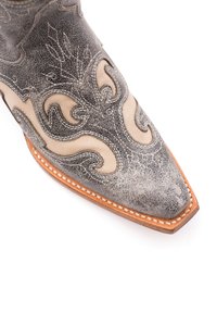 Stivale da cowboy in pelle grigia con motivi di cucitura ornati. Presenta una punta appuntita e una suola color tan con cuciture decorative.