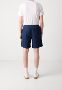 Námořnické džínové šortky s elastickým pasem, bočními kapsami a jednou zadní kapsou; nošeny s bílým tričkem a bílými teniskami.