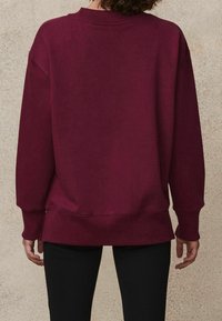 Burgunderfarbener Sweatshirt mit geripptem Rundhalsausschnitt und langen Ärmeln. Bietet eine lockere Passform, seitliche Schlitze und einen weichen, strukturierten Stoff.