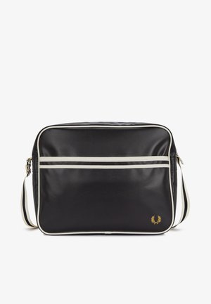 Czarna prostokątna torba na ramię z białym obramowaniem, przednią kieszenią na zamek, regulowanym paskiem i małym złotym logo w kształcie wieńca laurowego w prawym dolnym rogu.