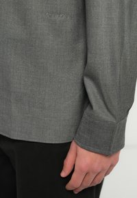 Sivá textúrovaná košeľa s dlhým rukávom, s jemným logom Calvin Klein na hrudi a elegantným dizajnom manžety.