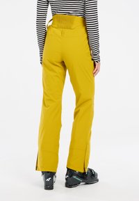 Geltoni slidinėjimo keliai, pagaminti iš patvarios medžiagos, su tamprių juostos, užtrauktukais ant kelnių apačios ir derinami su juodais slidinėjimo batais.