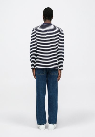 Striped long-sleeve shirt in navy and white, paired with loose-fitting blue jeans and white sneakers. Viewed from the back.