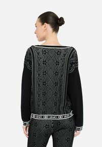 Dolcevita nero con intricati motivi grigi, scollatura ampia e finiture bianche con marchio. Texture morbida con maniche lunghe e vestibilità rilassata.