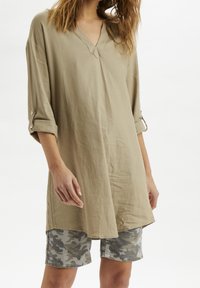 Khaki tuniek met een V-hals, driekwart mouwen met opgerolde manchetten, gecombineerd met camouflage shorts. Zacht, lichtgewicht materiaal met een losse pasvorm.