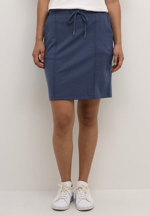 Blå stretchkjol i bomull med elastisk midja, dragsko och sidofickor. Kombinerad med vita sneakers. Enkel, avslappnad design.