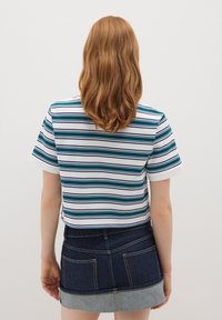 T-shirt a righe bianco, verde e blu, tagliato, con maniche corte, abbinato a una gonna di jeans con due tasche posteriori e orlo blu chiaro.