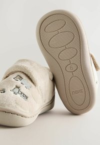 Chaussons pour tout-petits beige doux avec broderie de camion, l'un montrant une semelle texturée détaillée marquée taille 6 et la marque "next."