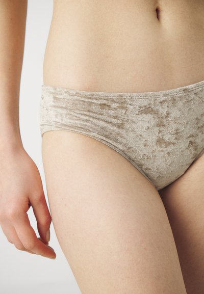 Gaiši bejžīgas samta bikini apakšbikses ar gludu tekstūru, kurām ir plata josta un maigais spīdums no auduma.