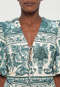 Virágmintás ruha, teal színű mintákkal, krém háttérrel, mély V-kivágással, elöl megkötős részlettel és puffos ujjal.