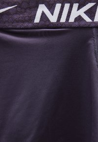 Κοντινό πλάνο ζώνης σκούρου αθλητικού ρουχισμού με υφή και μερικώς ορατό λευκό λογότυπο "NIKE".