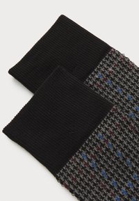Stickade strumpor med svart ribbad mudd, med en grå bas mönstrad med röda och blå diamantformer. Texturerad och lätt design.