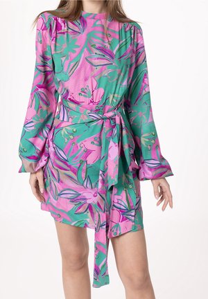 Donna che indossa un vestito a portafoglio a maniche lunghe, rosa e verde con fantasia floreale, cintura annodata in vita e orlo corto.