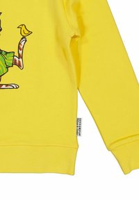 Gul sweatshirt med en grafisk av en tecknad djur som håller en gul fågel. Mjuk textur med ribbade muddarna. Etiketten syns vid fållen.