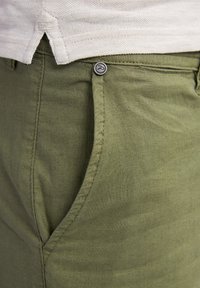 Olive green linen pants with a visible front pocket, metal button, and tonal stitching. Smooth texture and casual design.