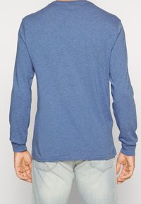 Långärmad, rundhalsad skjorta i heathered blått tyg. Mjuk textur, avslappnad passform, med färdigsydda fållar och ribbade muddar.