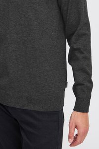 Tmavosivý sveter s rebrovaným lemom a manžetami, vyrobený z mäkkého pleteného materiálu. Detail švov a malá logo visačka na boku.